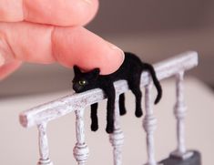 a hand holding a tiny black cat on top of a white railing with green eyes