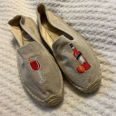 a pair of slippers with embroidered wine glasses on the front and bottom, sitting on a white blanket