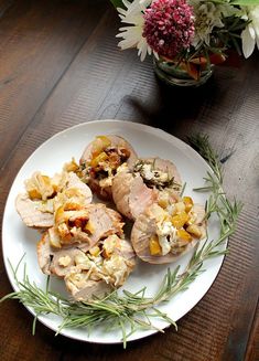 a white plate topped with meat covered in stuffing next to a vase filled with flowers