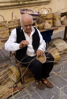 an old man sitting on a bench with some baskets in front of him and his hands