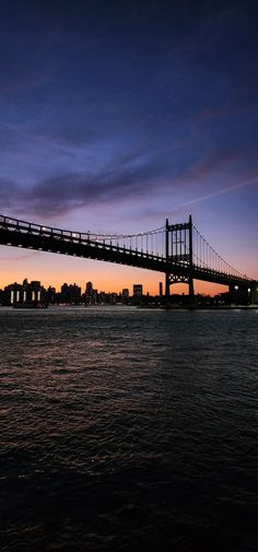 a bridge over water at sunset with buildings in the background and clouds in the sky