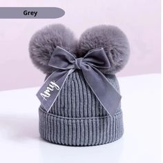 a gray hat with two pom poms on the top and a bow at the bottom