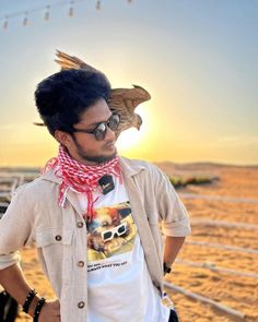 a man wearing sunglasses and a scarf standing in front of a fence with a bird on his head