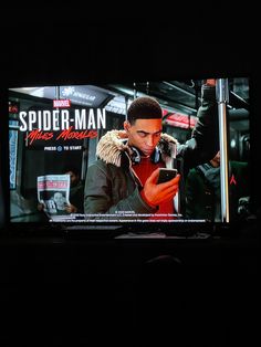 a television screen showing spider - man on it's display in the dark with people standing around