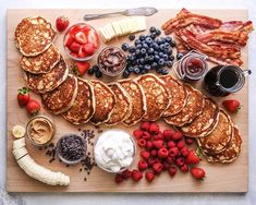 pancakes, strawberries, bananas, blueberries and other foods are arranged on a cutting board