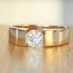 two gold wedding rings with a diamond on top of them, sitting on a wooden surface