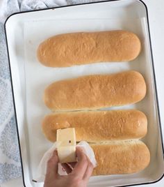 someone holding a piece of butter next to four long loafs of bread on a baking sheet