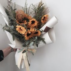 a bouquet of sunflowers and greenery wrapped in white paper with a ribbon