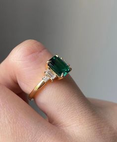 a woman's hand holding a ring with an emerald and diamond set in it