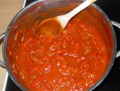 a large pot filled with red sauce on top of a stovetop next to a wooden spoon