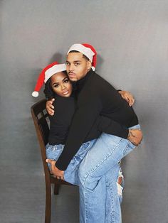 a man and woman sitting on top of a wooden chair wearing santa's hats