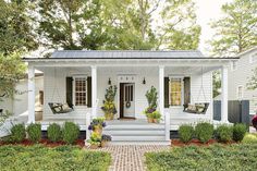 a white house with black shutters on the front porch and two plants in pots