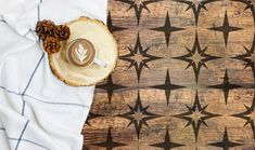 a cup of coffee sitting on top of a wooden table next to some pine cones