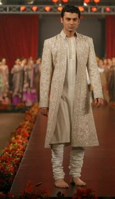 a man walking down a runway wearing a white suit