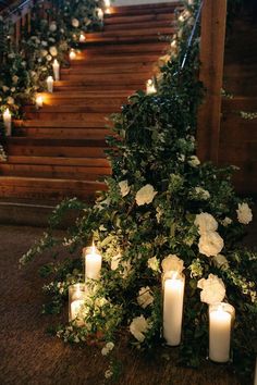 candles are lit on the ground in front of flowers and greenery with stairs leading up to them