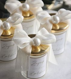 small white jars with gold lids and bows on them are decorated with pearls, satin ribbons and ribbon