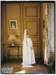 a woman in a white wedding dress standing in front of a painting on the wall