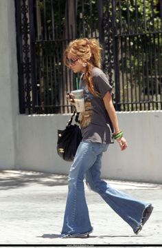 a woman walking down the street while using her cell phone and holding a purse with one hand