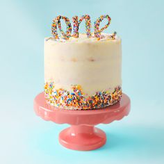 a white cake with sprinkles and the word one on top is sitting on a pink pedestal