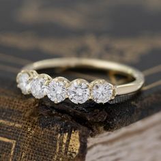 a five stone diamond ring sitting on top of a piece of wood with an old book in the background