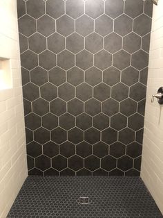 a black and white tiled bathroom with hexagonal tiles on the wall, shower head and floor