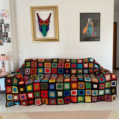 a multicolored crocheted couch sitting in a living room with pictures on the wall