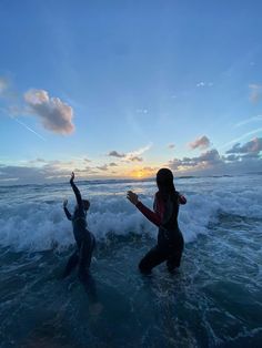 two people in wetsuits are standing in the ocean waves and one person is holding their arms up