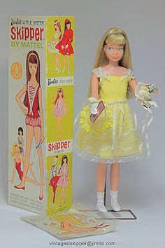 the doll is wearing a yellow dress and holding a flower in her hand while standing next to a cardboard box