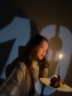 a woman holding a plate with a piece of cake on it and a lit candle