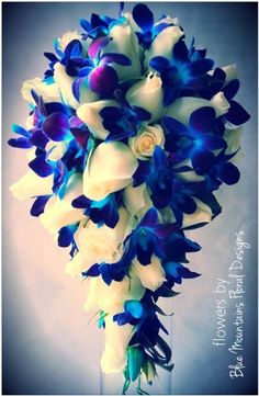 a bridal bouquet with blue and white orchids on the bottom, in a glass vase