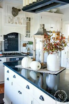 a kitchen with white cabinets and black countertops has pumpkins on the island in front of it