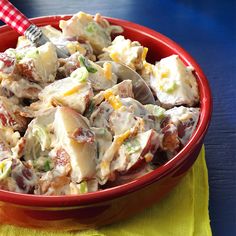 a red bowl filled with potato salad on top of a yellow napkin next to a fork