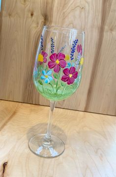 a wine glass with flowers painted on the side sitting on top of a wooden table