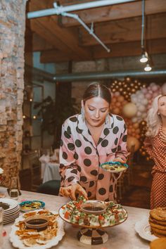 a woman standing in front of a table filled with plates of food and desserts