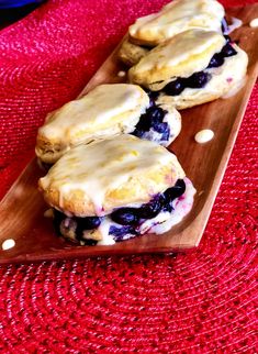 three cookies with blueberries and white icing on a wooden tray sitting on a red tablecloth