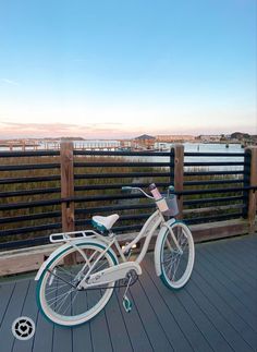 a white bicycle parked on top of a wooden deck next to a fence and water