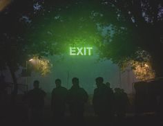 the exit sign is lit up at night with people standing under it and trees in the background