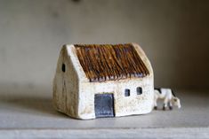 a small white house with a brown roof sitting on top of a table next to a cow