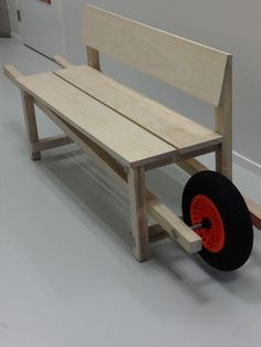 a wooden bench sitting on top of a white floor next to a black tire and red wheels