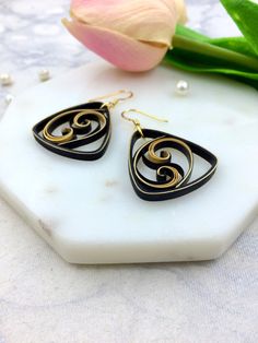 two black and gold earrings sitting on top of a white marble slab next to a tulip