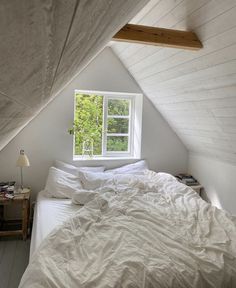 an unmade bed sitting under a window in a bedroom