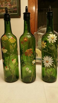 three green glass bottles with flowers painted on them sitting on a table next to a mirror