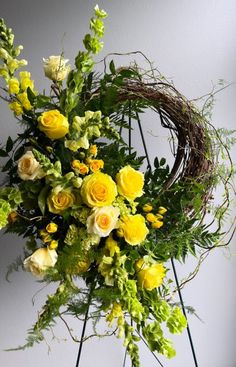 a wreath with yellow flowers and greenery hanging on a wall next to a white wall