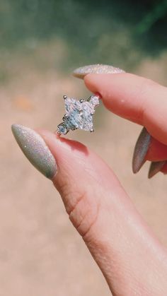 a woman's hand holding a ring with a diamond on it and glittery nails