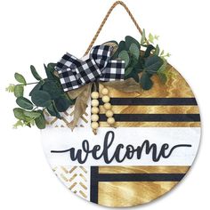 a welcome sign hanging on the side of a wall with greenery and berries around it