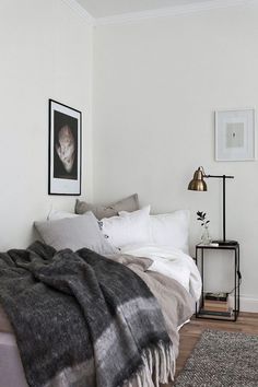 a bedroom with white walls and wood flooring has a large bed covered in blankets