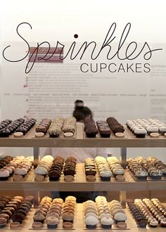 a display case filled with lots of different types of cupcakes on top of wooden shelves