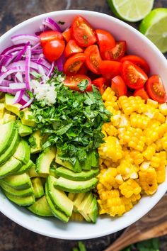 a white bowl filled with corn, avocado, tomatoes and red onion wedges