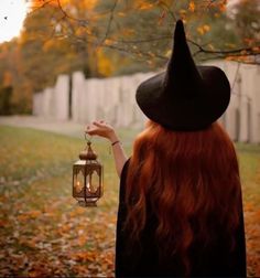 a woman with red hair wearing a witches hat and holding a lantern in her hand