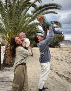 a man holding a baby while standing on top of a woman's shoulders next to a palm tree